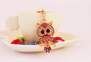 Detailed view of owl keychain with pink and purple rhinestones hanging over a tea cup