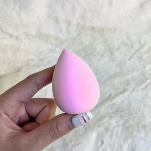 Close-up of a pink teardrop-shaped makeup sponge held by hand on a soft textured background
