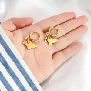Detailed macro view of 18K gold butterfly drop earrings held on a hand for size comparison
