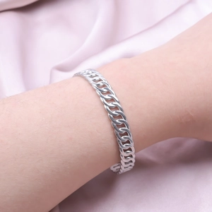 Detail view of a silver Cuban link chain bracelet worn on a wrist against silk background