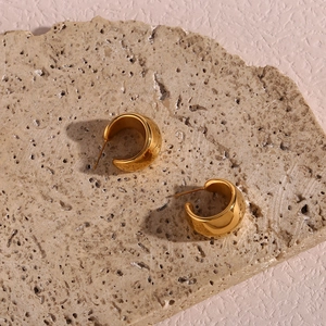 Détail de boucles d'oreilles créoles C dorées à facettes sur texture de pierre naturelle