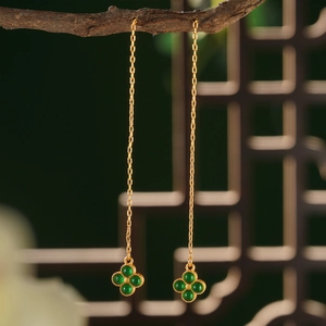 Detail of vintage gold earrings with green clover pendants on an artistic wood branch