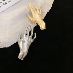 Polished hand shaped brooches in gold and silver finish on a stylish minimalist background