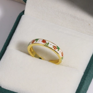 Detail of gold enamel ring with white red and green flower patterns on velvet