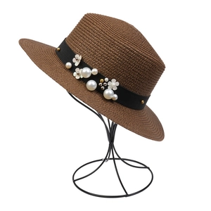 Detail of a brown woven sun hat featuring black ribbon with pearls and white floral accents