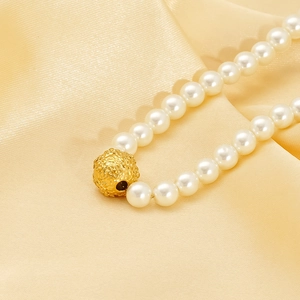Elegant pearl necklace featuring a floral textured gold bead on champagne satin background