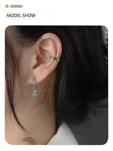 Model wearing silver emerald drop earrings and matching cuff set with green gemstones