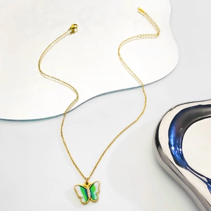 Detail shot of a golden butterfly pendant with green and white wings and inlaid zircons