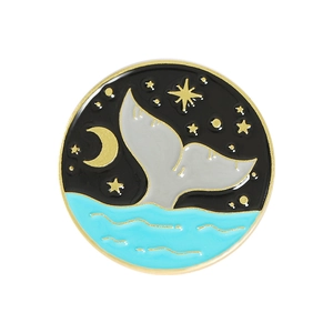 Macro detail of round whale tail enamel pin with golden crescent moon and waves