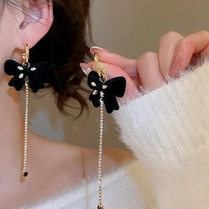 Detail of elegant black flocked bow earrings with gold tassels and sparkling rhinestones