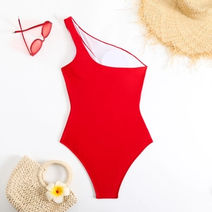 Flat lay of red one-shoulder swimsuit with summer holiday accessories on white background
