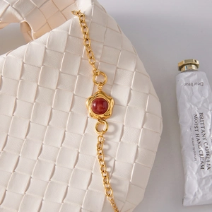 Detail of cream woven texture handbag with golden chain and ruby floral pendant