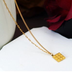 Detailed close-up of golden asymmetric chain necklace with geometric square pendant