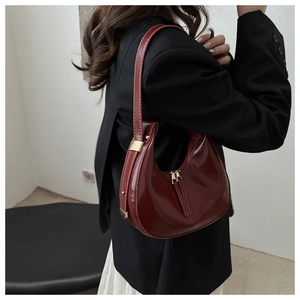 Side view of wine red glossy patent leather crescent shoulder bag with golden hardware