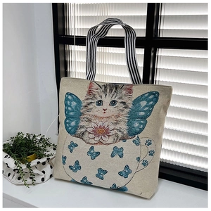 Detail of cream canvas tote bag featuring winged cat illustration and striped handles