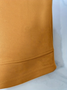 Close-up of ginger yellow knit fabric showing precise double-needle stitching on the hem