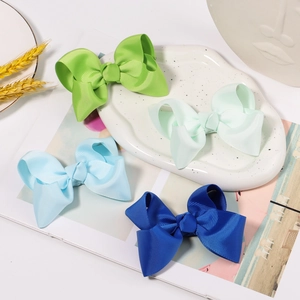 Grosgrain ribbon hair bows in green and blue shades displayed on a ceramic tray