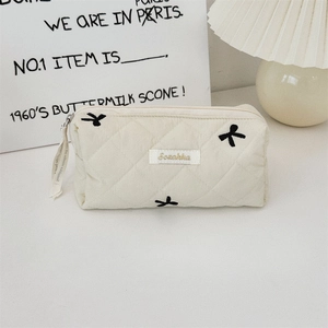 Detailed view of beige quilted makeup bag with black bow embroidery and top zipper
