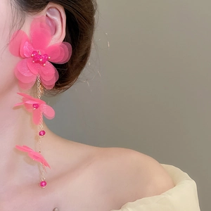 Close-up of pink chiffon flower fringe earrings worn by a model in soft lighting