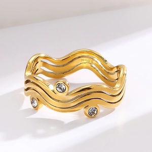 Modern gold wavy stainless steel ring with three clear crystals on a minimalist background