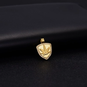 Makroaufnahme von Goldschild-Anhänger mit geprägtem Hanfblatt und Kristallkranz