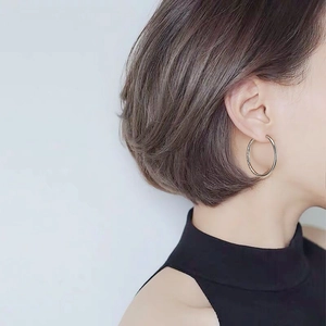 Close-up of a large polished silver hoop earring worn by a model in a minimalist style