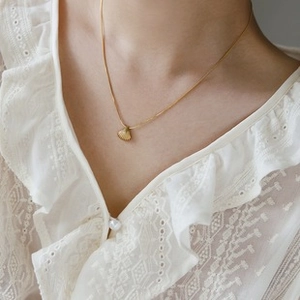 Close-up of gold titanium steel necklace with shell texture fan pendant on white lace