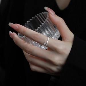 Close-up of a silver-plated H-shaped ring with pavé zircons on a model holding glass