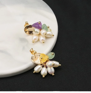 Macro detail of handmade gold-plated earrings with natural pearls and colorful gemstones