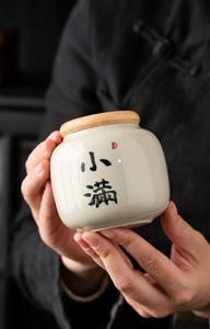 Close-up of small ceramic tea canister with calligraphy held in hands for portability