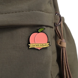 Detailed enamel peach pin on an olive green canvas backpack as a stylish accessory