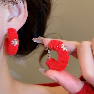 Macro detail of red flocked hoop earrings with golden snowflake charm for winter