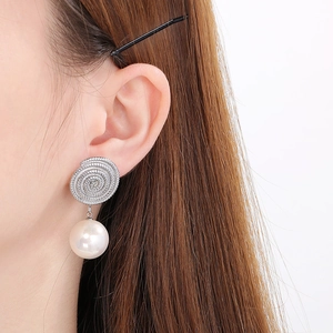 Close-up of elegant spiral stainless steel earrings with white pearl pendants on model