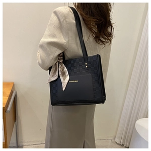 Detail of black woven tote bag with silk scarf charm worn by model in beige suit