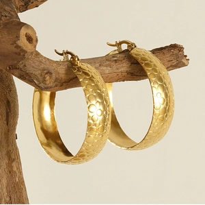 Detailed view of 18K gold plated hoop earrings with embossed circular texture on wood