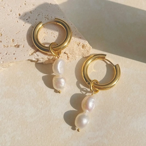 Detail of gold hoop earrings with double baroque pearls on textured stone background