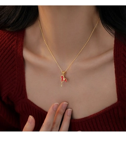 Detailed view of a gold-plated horse pendant with red enamel and zircon on a model