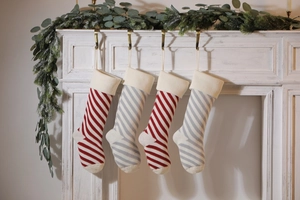 Close-up of red and grey knitted Christmas stockings hanging on a white mantel with greenery
