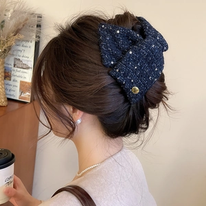 Detail of tweed bow hair claw clip in navy blue with sequins worn by a model