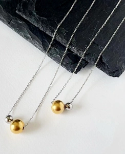 Detail of minimalist 18k gold and silver bead pendants on slender titanium steel chains