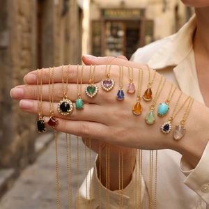 Detailed view of heart and geometric gemstone necklaces displayed on hand in sunlight