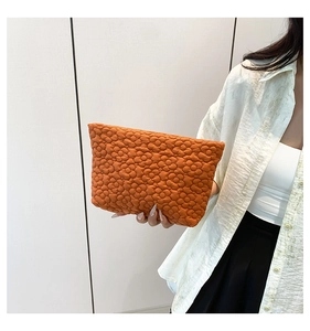 Detail view of orange quilted floral clutch bag showing 3D petal texture and soft fabric