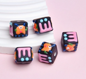 Detail shot of five black resin square beads with colorful cartoon monster carvings