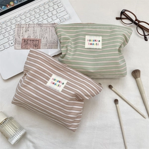Detail of striped fabric makeup bags with zipper closure and brand label on white fabric
