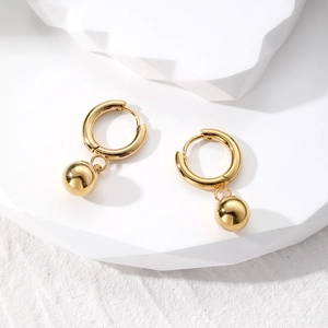 Macro detail of golden irregular oval hoop earrings with spherical pendant on white blocks