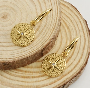 Vue détaillée de boucles d'oreilles étoile dorées 18 carats avec zircon sur du bois