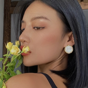 Elegant round resin stud earrings with pearl luster and gold metal rim on a model