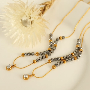 Elegant gold snake chain necklace with faceted grey beads and crystal pendants on white background