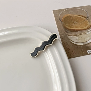 Detail of a wavy checkerboard hair clip in black marble texture on a white tray