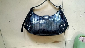 Detail view of black crocodile pattern faux leather handbag with silver rivets and buckle